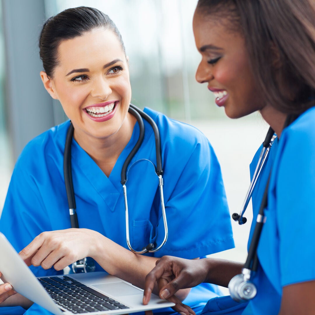 Nurse pointing at laptop while communicating with colleague.